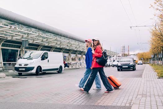 Two happy girls walking near airport, with luggage. Air travel, summer holiday.