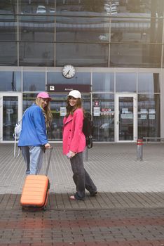 Two happy girls walking near airport, with luggage. Air travel, summer holiday.