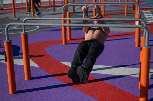 Shirtless man doing horizontal balance on parallel bars at sports ground