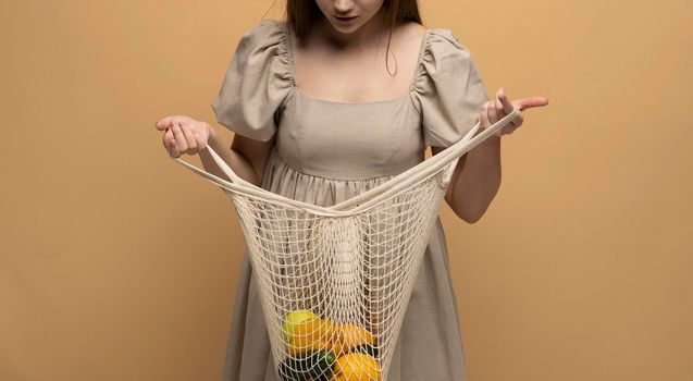 Attractive brunette woman holding a open mesh grocery bag with vegetables. Concept of no plastic. Zero waste, plastic free. Eco friendly concept. Sustainable lifestyle