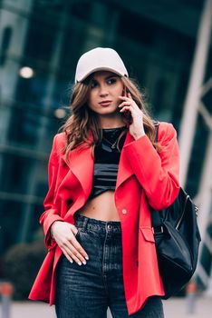 Stylish woman on the street uses a mobile phone. beautiful woman with long dark hair in a red jacket, black top and a cap