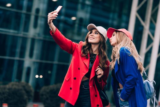 Two joyful cheerful girls taking a selfie while standing together at street near the mall.