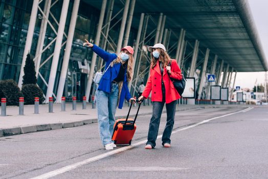 Two happy girls walking near airport, with luggage. Air travel, summer holiday