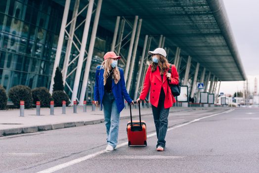 Two happy girls walking near airport, with luggage. Air travel, summer holiday