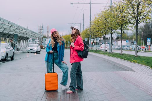 Two happy girls walking near airport, with luggage. Air travel, summer holiday.