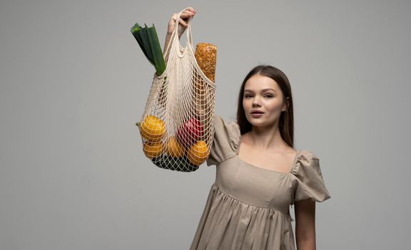 Brunette woman showing a reusable mesh shopping bag full of fresh groceries. Zero waste. Ecologically and environmentally friendly packets. Canvas and linen fabrics. Save nature concept