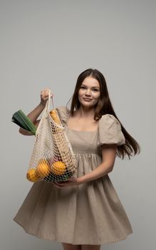 Young woman in a summer dress holding reusable cotton shopping mesh bag with groceries from a market. Concept of no plastic. Zero waste, plastic free. Eco friendly concept. Sustainable lifestyle