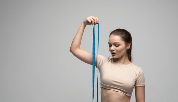 Gorgeous healthy young brunette woman in fitness outfit holding a measure tape. Beauty and health concept. Health care and healthy nutrition. Perfect slim body. Weight loss and diet concepts