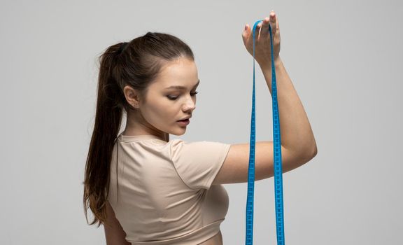 Weight loss and diet concepts. Beautiful young brunette woman in fitness outfit holding a measure tape. Beauty and health concept. Health care and healthy nutrition