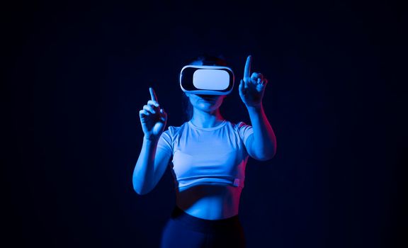 Modern architect using virtual reality glasses at workplace. Woman working in VR goggles in neon light. Designer working in VR studio