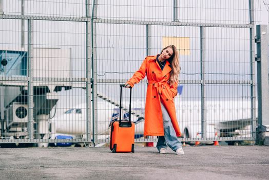 happy woman walking near airport, with luggage. Air travel, summer holiday. dressed in orange trench. Airport on a background