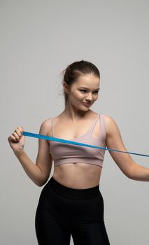Happy attractive brunette woman with a perfect sexy body in beige top sportswear holding a blue measuring tape. Weight loss and diet concepts. Health care and healthy nutrition. Perfect slim body
