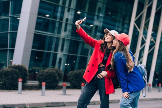 Two joyful cheerful girls taking a selfie while standing together at street near the mall