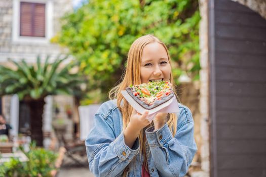 Young woman tourist eating traditional pizza in the old town of Budva. Travel to Montenegro concept.