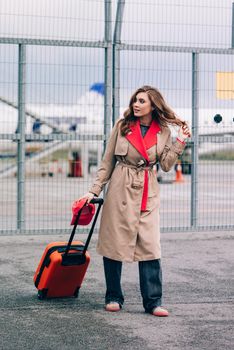 happy woman walking near airport, with luggage. Air travel, summer holiday. dressed in beige trench. Airport on a background