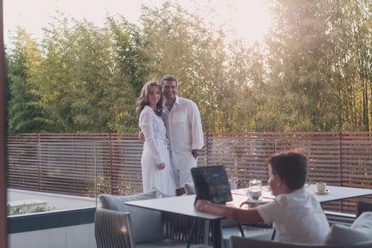 Happy elderly couple resting on the balcony of a luxury house while their son using a tablet. Selective focus. High-quality photo