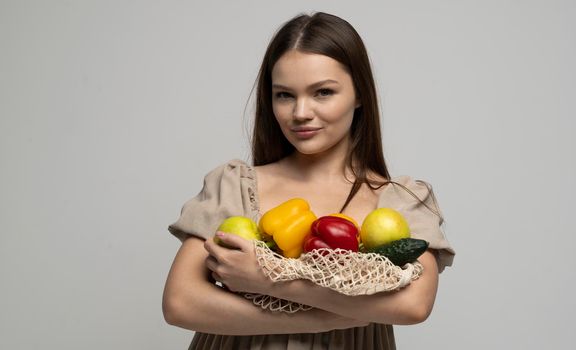 Beautiful attractive happy brunette woman holding mesh grocery bag with vegetables. Concept of no plastic. Zero waste, plastic free. Eco friendly concept. Sustainable lifestyle