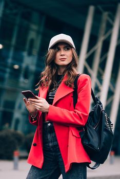 Stylish woman on the street uses a mobile phone. online shopping. use of mobile applications. beautiful woman with long dark hair in a red jacket, black top and a cap