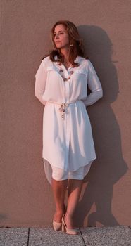 A modern elderly woman in a white dress stands on the roof of the house and enjoys the sunset. Selective focus. High-quality photo