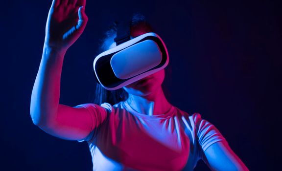 Virtual reality technology concept. Portrait of young woman stands in studio wearing VR glasses and swiping scrolling with hand in air