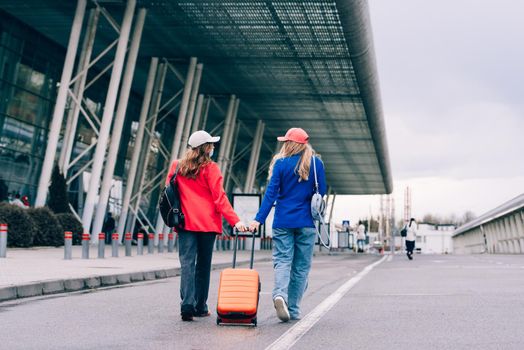 Two happy girls walking near airport, with luggage. Air travel, summer holiday. View from the back