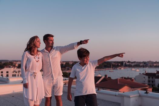 The happy family enjoys and spends time together on the roof of the house while watching the sunset on the open sea together. High-quality photo