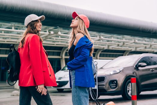 Two happy girls walking near airport, with luggage. Air travel, summer holiday.