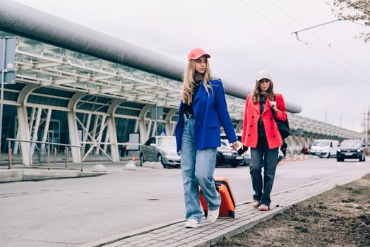 Two happy girls walking near airport, with luggage. Air travel, summer holiday.