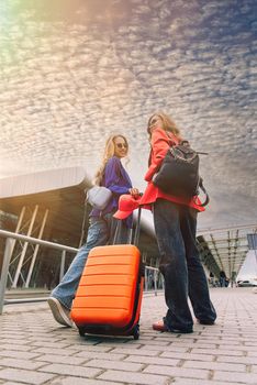 Two happy girls walking near airport, with luggage. Air travel, summer holiday. View from the back