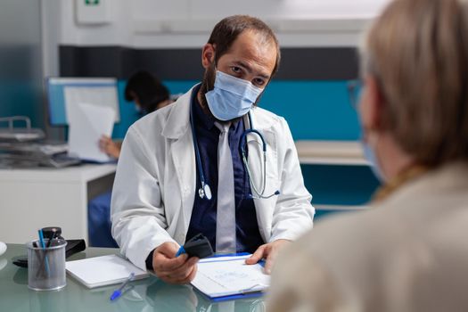 Doctor putting medical seal on prescription paper, giving medicine to senior patient at examination. General practitioner using stamp on consultation report during covid 19 pandemic.