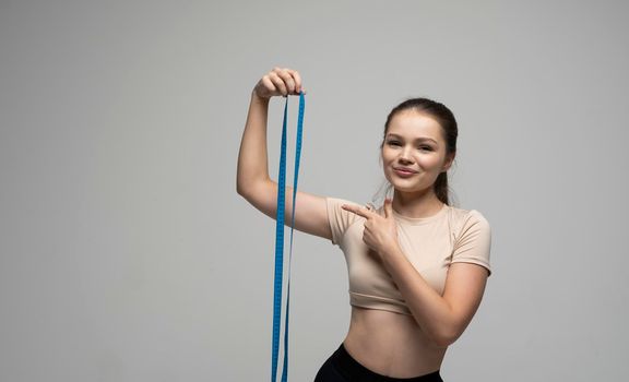 Gorgeous beautiful attractive happy healthy young brunette woman in fitness outfit holding a blue measure tape