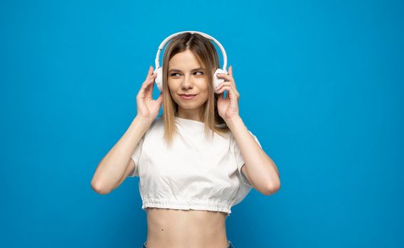 Beautiful young woman in headphones listening to music blue background. Young beautiful woman in bright outfit enjoying a music