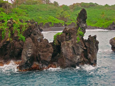 Visitors Explore the Black Basaltic Magma or Basalt Lava Cliffs at Waianapanapa State Park in Hana, Hawaii on the island of Maui