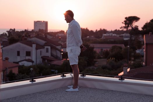an elderly businessman in casual clothes enjoys the roof of his house at sunset time. Selective focus. High-quality photo