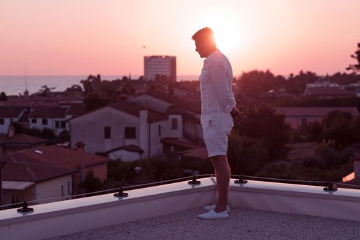 an elderly businessman in casual clothes enjoys the roof of his house at sunset time. Selective focus. High-quality photo