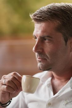 A senior businessman in casual clothes sits on the terrace of a luxury house and drinks morning coffee. Selective focus. High-quality photo