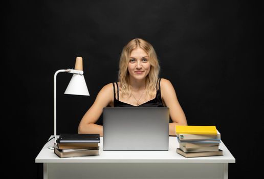 Excited young woman working with a grey laptop computer, notebook while sitting at the table. Smiling business woman or student received a good news isolated on a black background
