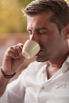 A senior businessman in casual clothes sits on the terrace of a luxury house and drinks morning coffee. Selective focus. High-quality photo