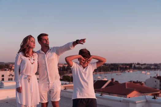 The happy family enjoys and spends time together on the roof of the house while watching the sunset on the open sea together. High-quality photo