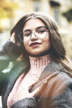 young beautiful girl posing on the street. Dressed in a stylish gray coat and knitted pink sweater.