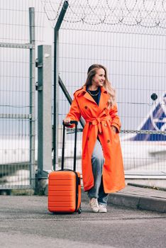 happy woman walking near airport, with luggage. Air travel, summer holiday. dressed in orange trench. Airport on a background