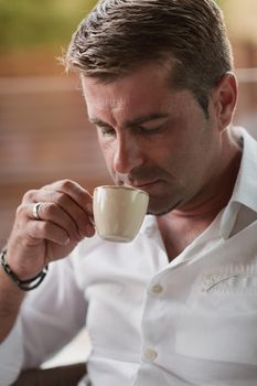 A senior businessman in casual clothes sits on the terrace of a luxury house and drinks morning coffee. Selective focus. High-quality photo