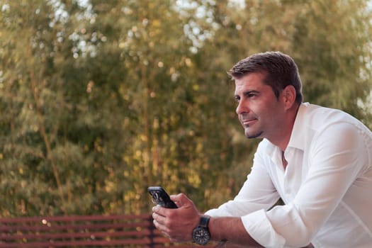 A businessman in casual clothes resting on the balcony of the terrace while using a smartphone. Selective focus. High-quality photo