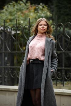 young beautiful girl posing on the street. Dressed in a stylish gray coat, knitted pink sweater and skirt.