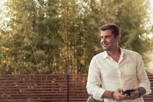 A businessman in casual clothes resting on the balcony of the terrace while using a smartphone. Selective focus. High-quality photo