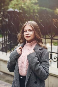 young beautiful girl posing on the street. Dressed in a stylish gray coat, knitted pink sweater and skirt.