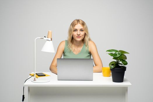 Smiling business woman working with a laptop isolated on a grey background. Portrait of a pretty young woman studying while sitting at the table with grey laptop computer, notebook