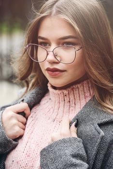 young beautiful girl posing on the street. Dressed in a stylish gray coat, knitted pink sweater and skirt.
