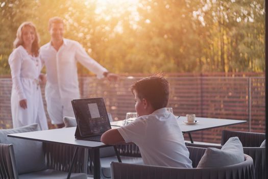 Happy elderly couple resting on the balcony of a luxury house while their son using a tablet. Selective focus. High-quality photo