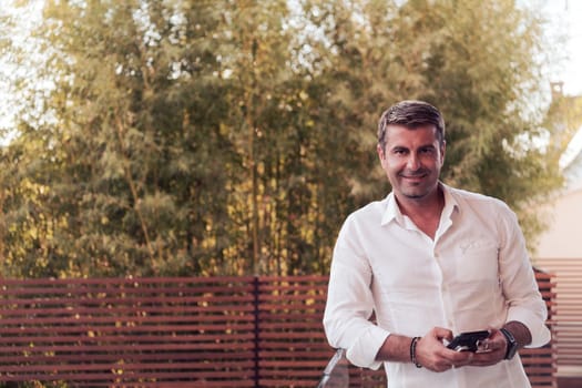 A businessman in casual clothes resting on the balcony of the terrace while using a smartphone. Selective focus. High-quality photo